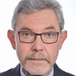 Portret mężczyzny w okularach, ubrany w garnitur i koszulę z krawatem, z siwymi włosami i wąsami, na białym tle.