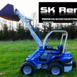 Niebieska, kompaktowa ładowarka kołowa marki Marim na zielonym trawniku, z logo firmy SK Rent w tle.