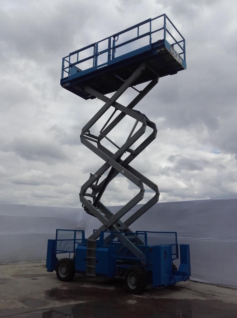 Niebieski podnośnik koszowy typu nożycowego na betonowym podłożu, z szarym niebem w tle.