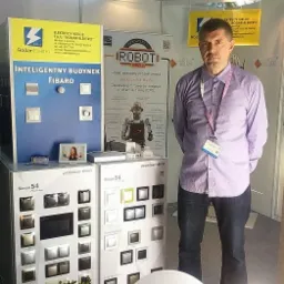 Stoisko z ekspozycją inteligentnych systemów Fibaro i osprzętu Simon 54 na targach. Mężczyzna w koszuli, prezentacja oferty Rodar-Elektro.