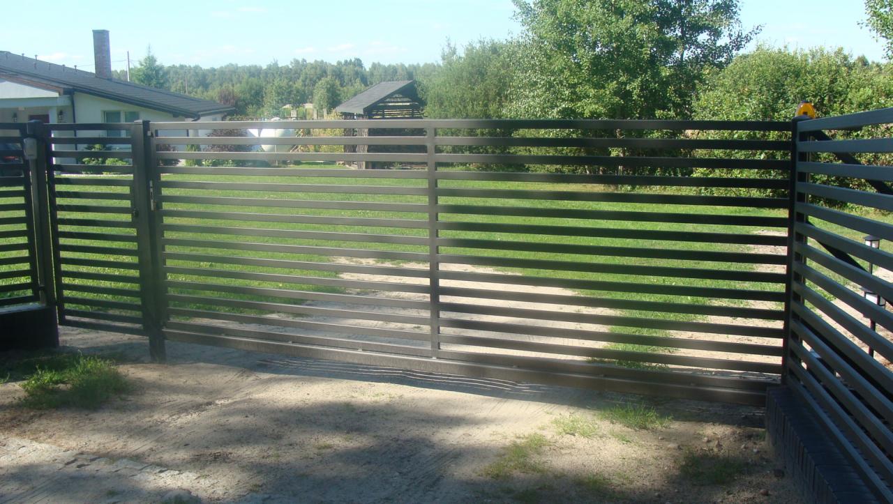 Nowoczesna, pozioma brama wjazdowa z metalowych profili, pomalowana na szaro, z widocznym domem i zielonym trawnikiem w tle.