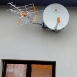 Antena satelitarna i antena naziemna zamontowane na jasnej ścianie budynku nad oknem z ciemną ramą.