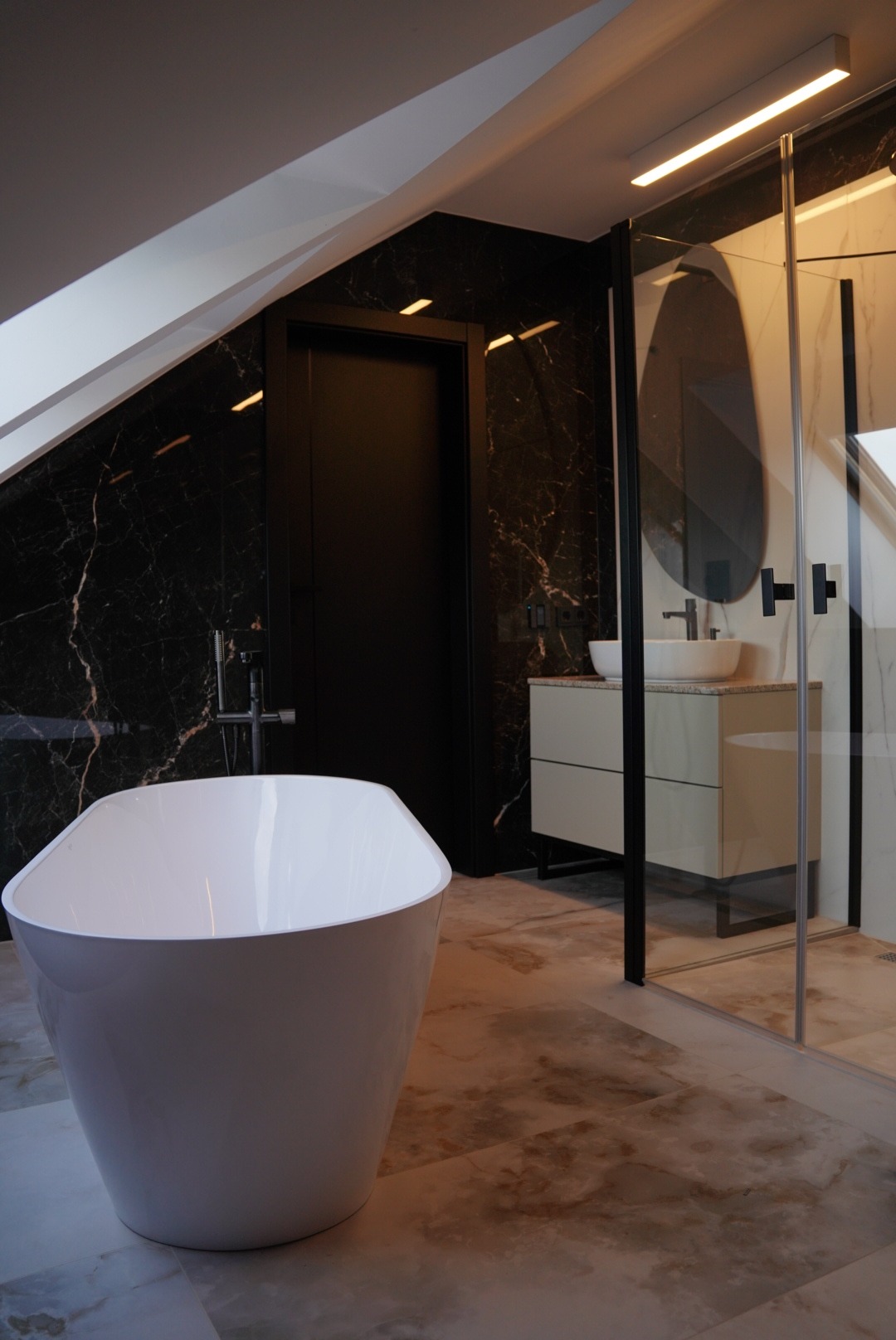 Nowoczesna łazienka w odcieniach bieli i czerni z wolnostojącą wanną, kabiną prysznicową ze szklanymi ścianami i umywalką na szafce, wykończona marmurem.