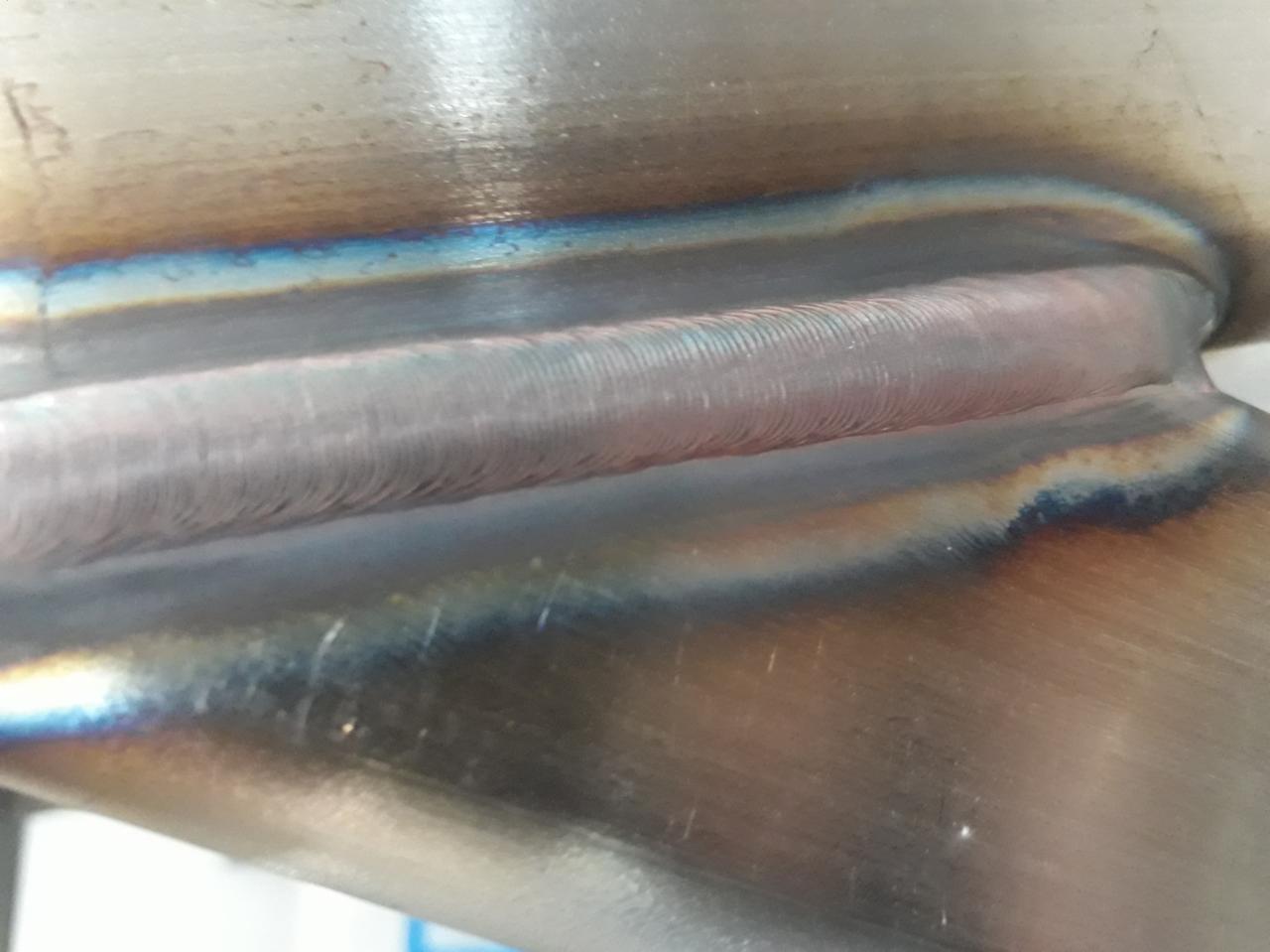 Szczegółowe zbliżenie spoiny rurociągu wykonanej w Suchym Dębie, widoczne tęczowe przebarwienia termiczne na metalu.