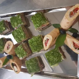 Srebrna taca z roladkami z tortilli z nadzieniem i kanapkami pokrytymi zieloną posypką, udekorowana listkami mięty i borówkami.