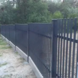 Nowoczesne, metalowe ogrodzenie panelowe w kolorze grafitowym, z podmurówką betonową, widok z boku, w tle zieleń i czerwony samochód.