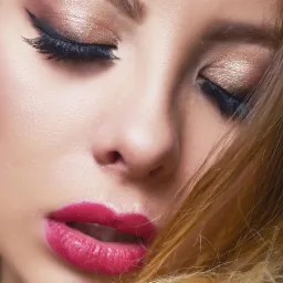 Portret zbliżeniowy kobiety z zamkniętymi oczami, widoczny intensywny makijaż oczu z czarnym eyelinerem i złotymi cieniami, pełne usta pomalowane na intensywny różowy kolor, kosmyki blond włosów...