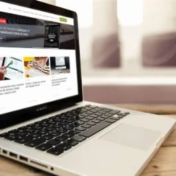 Laptop MacBook Pro wyświetlający stronę internetową firmy Comdrev na drewnianym biurku, z widocznymi aktualnościami i studium przypadku.