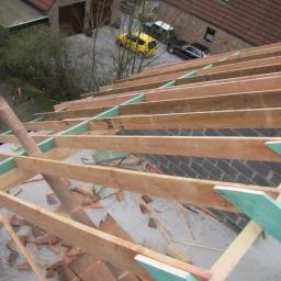 Grzegorz Miśta MasterDach - Konstrukcja drewniana dachu w trakcie budowy, widok z góry na więźbę z elementami zielonej izolacji, w tle domy i samochody.