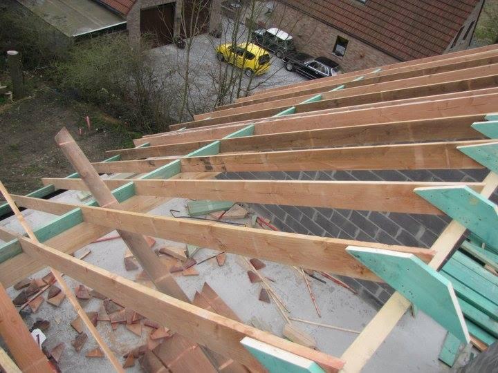 Konstrukcja drewniana dachu w trakcie budowy, widok z góry na więźbę z elementami zielonej izolacji, w tle domy i samochody.