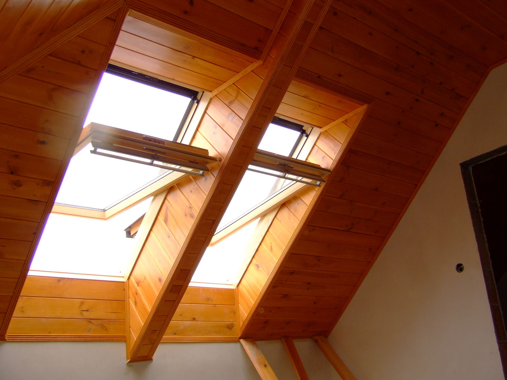 Poddasze wykończone boazerią z dwoma oknami dachowymi z widocznymi mechanizmami otwierania, jasne wnętrze.