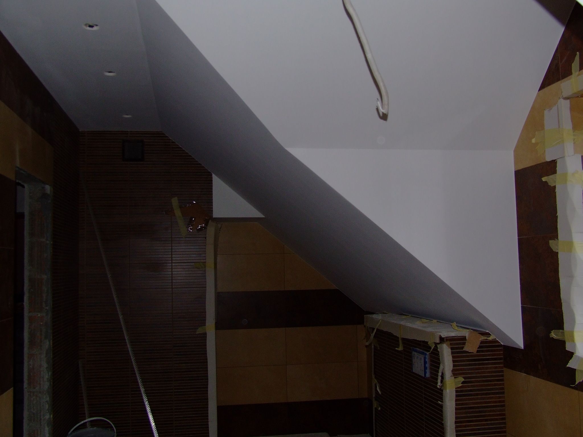 Docieplone poddasze z gładzią na skośnej ścianie, widoczne fragmenty instalacji elektrycznej i zabezpieczone taśmą malarską elementy wykończeniowe.