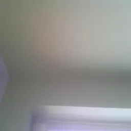 Świeżo pomalowany sufit i fragment ściany w jasnym, neutralnym odcieniu, widoczne rolety okienne w dolnej części kadru.