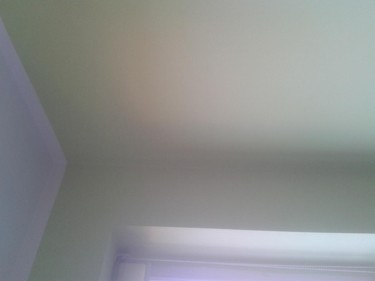 Świeżo pomalowany sufit i fragment ściany w jasnym, neutralnym odcieniu, widoczne rolety okienne w dolnej części kadru.