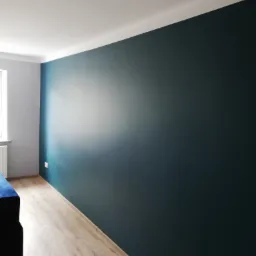 Świeżo pomalowana ściana w odcieniu głębokiego granatu, z widoczną fakturą farby, kontrastująca z jasną podłogą z paneli i fragmentem niebieskiej sofy w rogu.