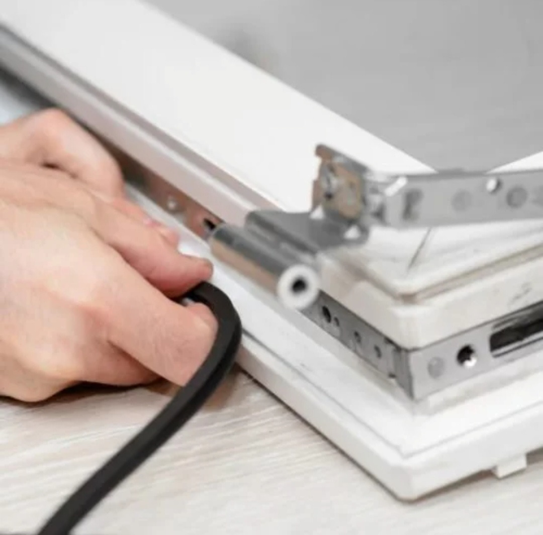 Uszczelnianie okna w Toruniu: dłoń wkłada czarną gumową uszczelkę w ramę okienną z metalowymi okuciami.