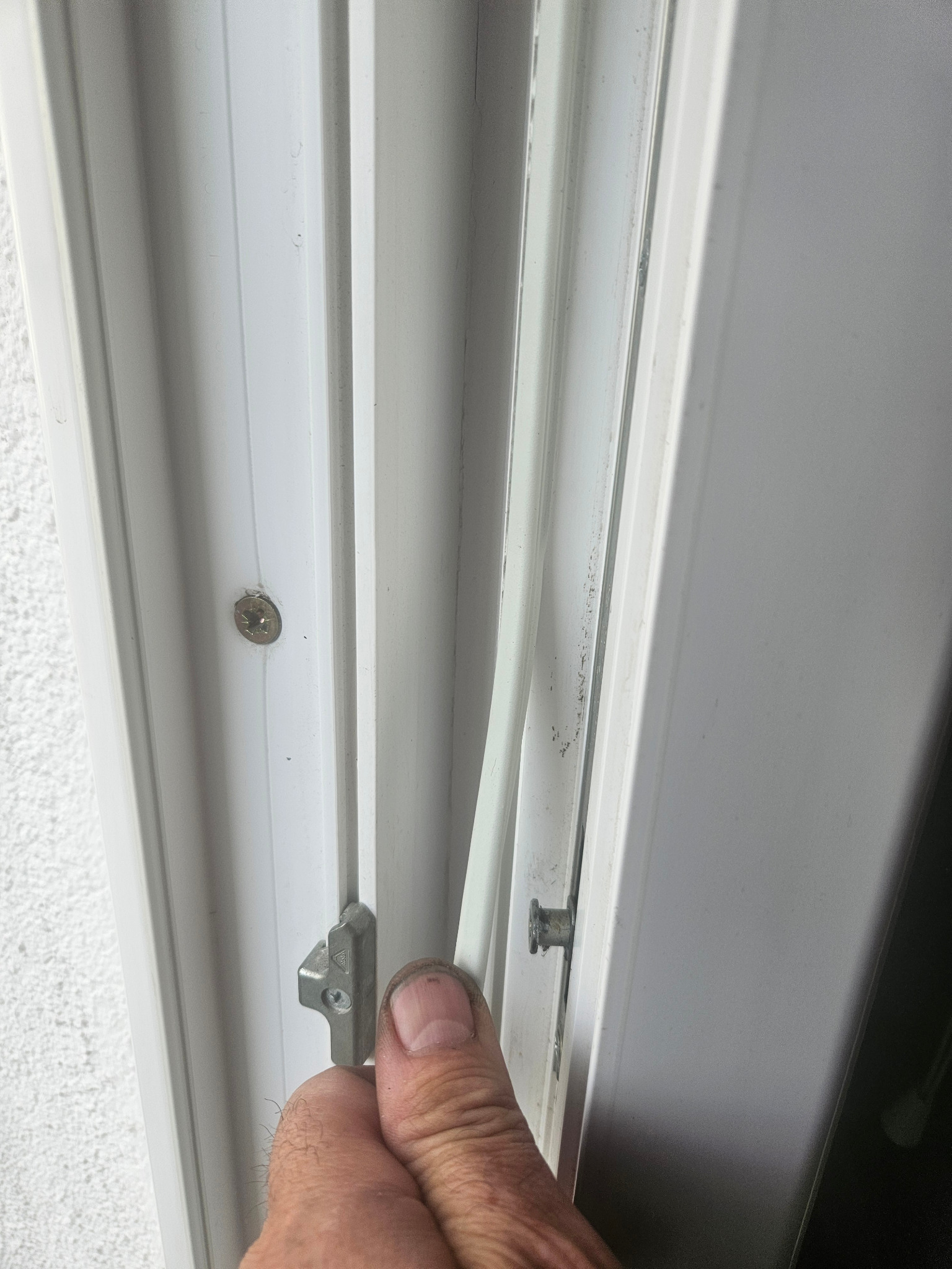 Białe okno PCV w trakcie regulacji. Widoczny mechanizm okienny i dłoń montera. Detal okna z bliska, oświetlenie dzienne.