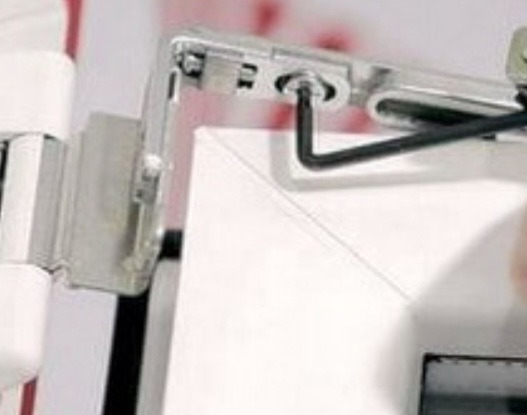 Regulacja okna PCV kluczem imbusowym. Detal mechanizmu okiennego w trakcie serwisu, widoczny biały profil okienny i narzędzie.