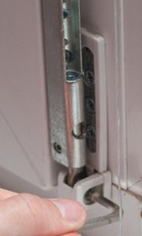 Regulacja zawiasu okiennego kluczem imbusowym. Widoczny mechanizm okna, śruby mocujące i dłoń montera. Detal naprawy okna PCV.