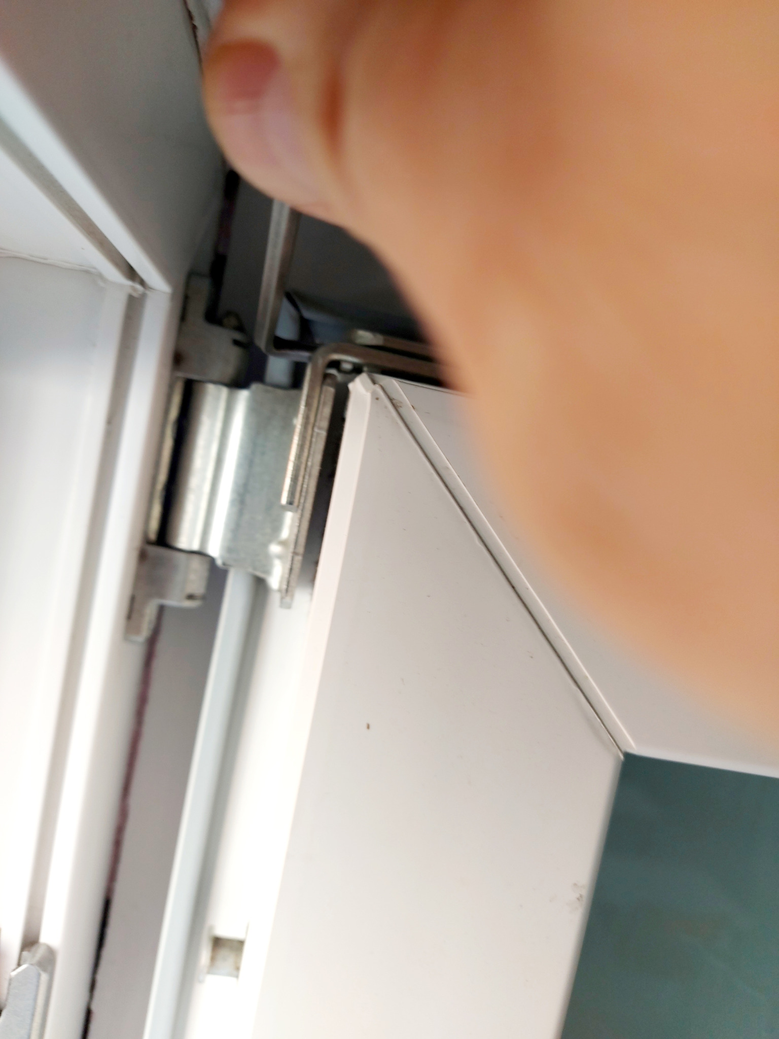 Detal okucia okiennego z białego PCV, widoczny fragment dłoni. Ujęcie z bliska, ukazujące mechanizm zawiasu.