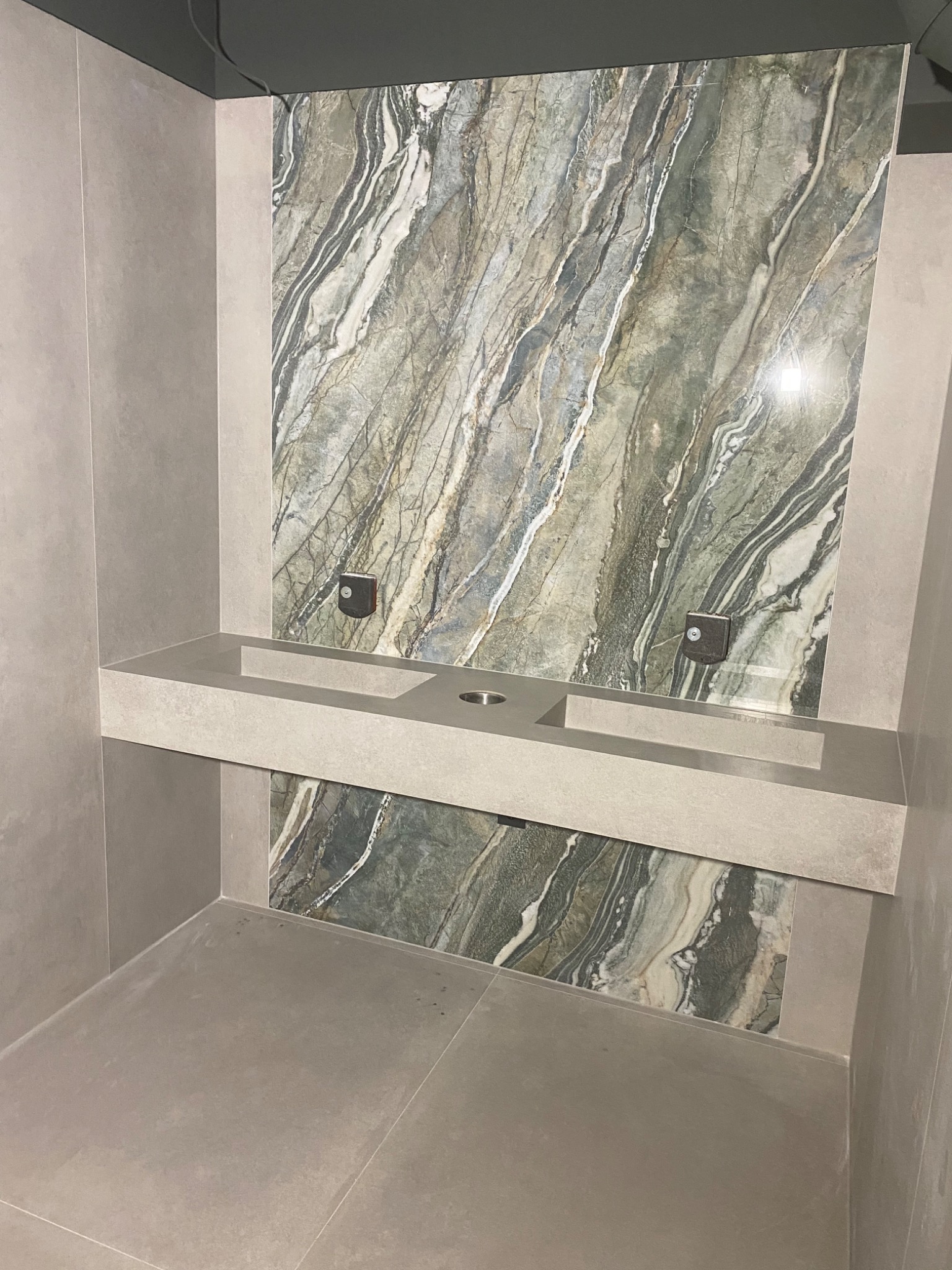 Wykończona łazienka w Lęborku z umywalką wpuszczoną w blat z szarego kamienia i okładziną ścienną z płytek imitujących marmur w odcieniach zieleni i szarości.