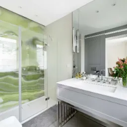 Nowoczesna łazienka z zielonym onyksem w kabinie prysznicowej, białą umywalką na metalowej konstrukcji i dużym lustrem.