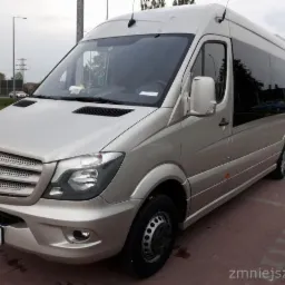 Złoty bus Mercedes-Benz Sprinter z przyciemnionymi szybami, zaparkowany na kostce brukowej, widok z przodu i boku.