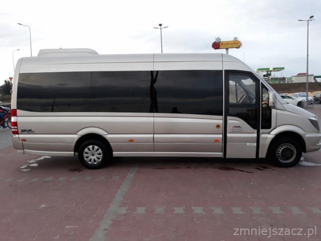 Srebrny bus z przyciemnianymi szybami na parkingu, w tle widoczny znak Biedronki.