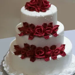 Trzypiętrowy tort ślubny z białym lukrem i dekoracjami z czerwonych róż z lukru, umieszczony na białej podkładce z koronkowym obrzeżem.