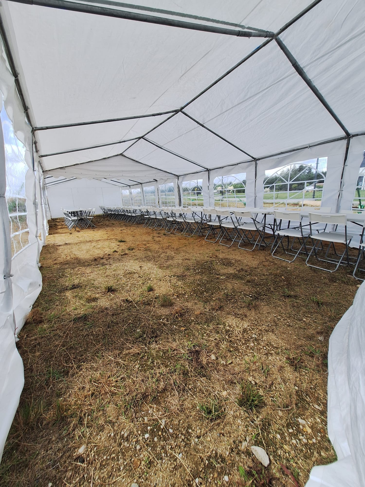 Wnętrze białego namiotu imprezowego z rzędami krzeseł i stołów, widok z perspektywy szerokokątnej, ukazujący konstrukcję i otoczenie.