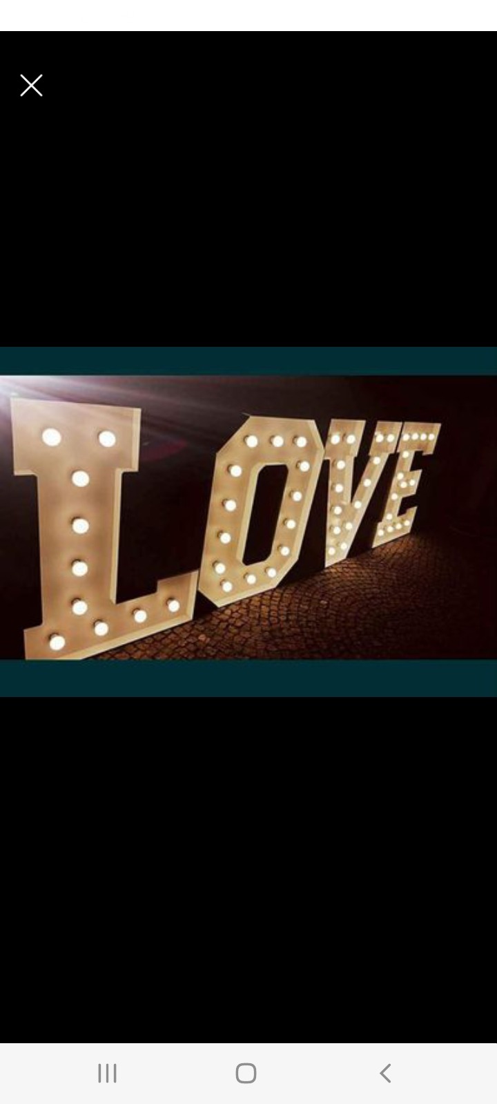 Dekoracyjny napis LOVE z żarówkami na ciemnym tle, ustawiony pod kątem. Idealny na ślub, walentynki lub inne romantyczne okazje. Ciepłe światło żarówek.