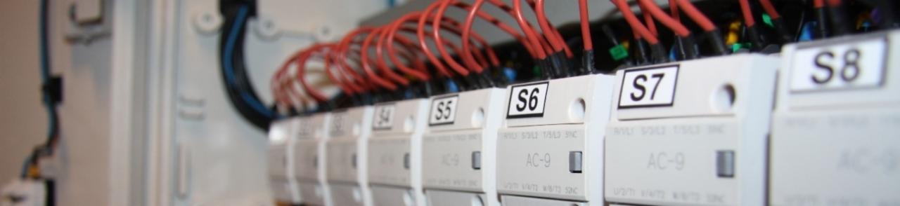 Szczegółowe ujęcie rozdzielnicy elektrycznej z widocznymi bezpiecznikami oznaczonymi S4, S5, S6, S7, S8, podłączonymi czerwonymi przewodami.