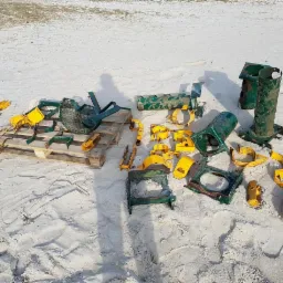 Elementy metalowe konstrukcji placu zabaw, częściowo pomalowane na żółto i zielono, rozłożone na piasku i palecie, prawdopodobnie po usunięciu starej powłoki.