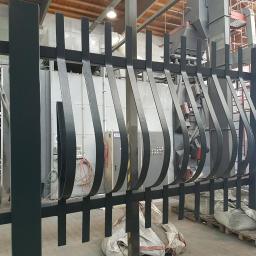 Sabbia Zabezpoeczenia Antykorozykne - Metalowa barierka po malowaniu proszkowym, w tle pracownik na drabinie i piec do malowania.