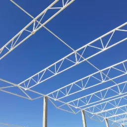 Widok z dołu na białą, pomalowaną proszkowo konstrukcję stalową z betonowymi słupami na tle błękitnego nieba.