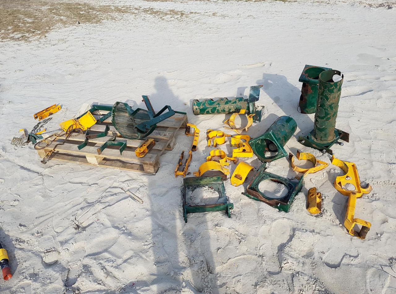 Elementy metalowe konstrukcji placu zabaw, częściowo pomalowane na żółto i zielono, rozłożone na piasku i palecie, prawdopodobnie po usunięciu starej powłoki.