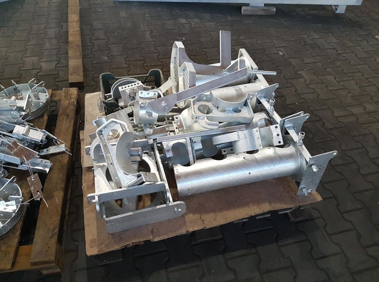 Metalowe elementy konstrukcyjne po obróbce, ułożone na palecie z drewna. Widoczne ślady po procesie obróbki, jasnoszary kolor metalu.