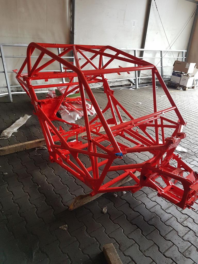 Czerwona, pomalowana proszkowo rama pojazdu buggy w Rzeczycy, umieszczona na drewnianych klockach, widoczna w warsztacie.