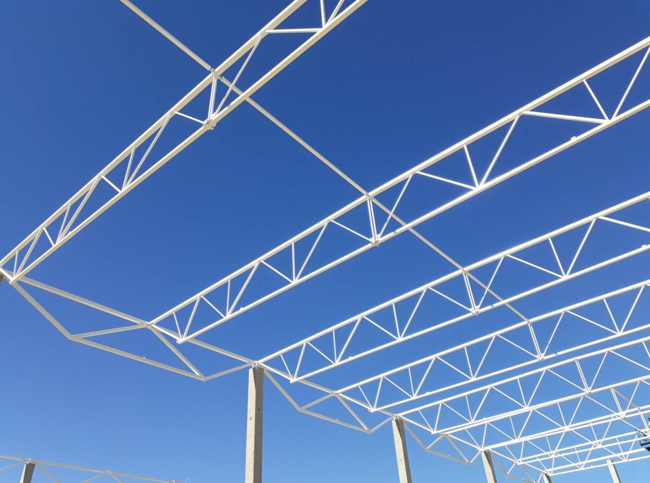 Widok z dołu na białą, pomalowaną proszkowo konstrukcję stalową z betonowymi słupami na tle błękitnego nieba.