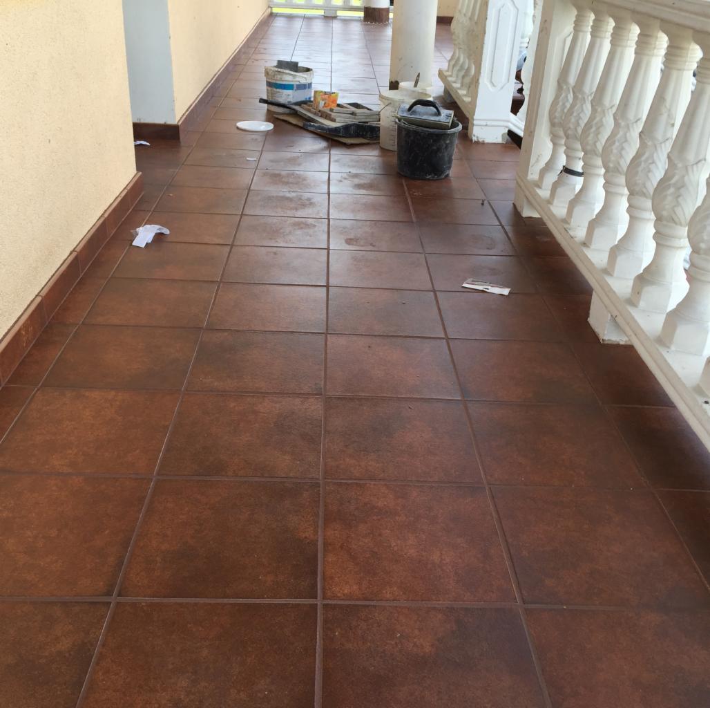 Brązowa terakota na zewnątrz, widoczne ślady po malowaniu, wiadro, kuweta i pędzle malarskie, biała balustrada w tle.