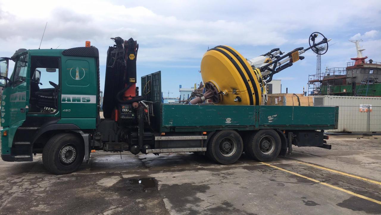 Transport ciężarowy w Łęgowie: Zielona ciężarówka Volvo z dźwigiem przewozi dużą, żółto-czarną boję nawigacyjną.