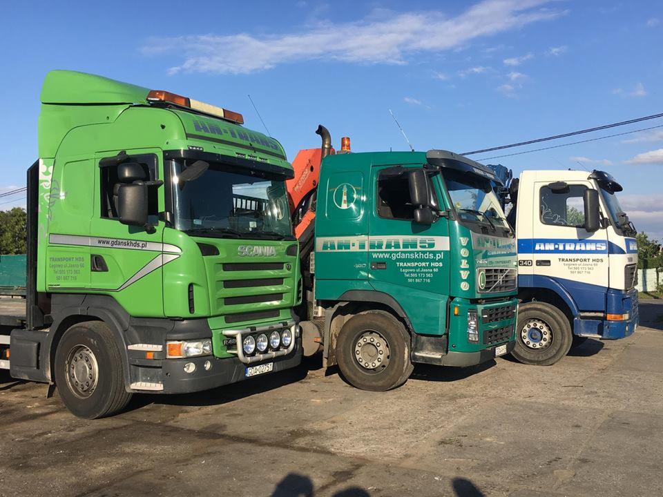 Trzy ciężarówki: zielona Scania z dodatkowymi reflektorami, turkusowa Volvo z dźwigiem HDS i biało-niebieska innej marki, zaparkowane obok siebie na placu, widoczne logo firm.