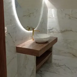 Nowoczesna łazienka z umywalką nablatową, złotą baterią i okrągłym lustrem z podświetleniem LED, wykończona płytkami imitującymi marmur.