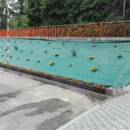 Skarpa zabezpieczona zieloną siatką z posadzonymi roślinami, obłożona donicami z kwiatami, widok z góry na betonową ażurową nawierzchnię.