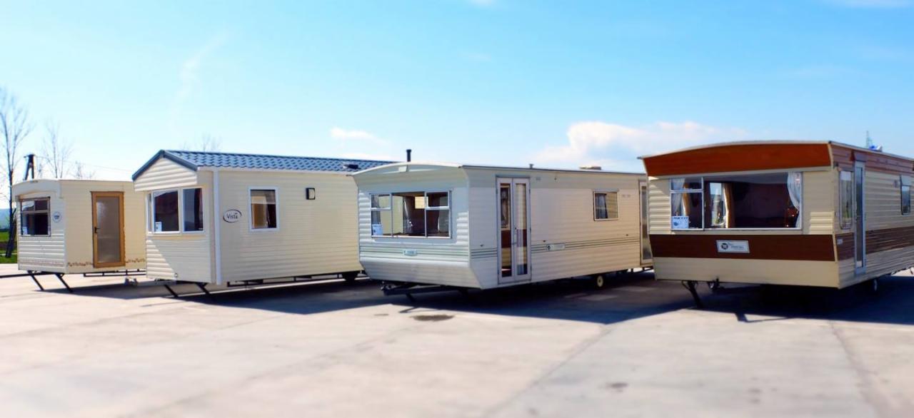 Cztery mobilne domki letniskowe o różnej stylistyce ustawione na betonowym placu w słoneczny dzień.