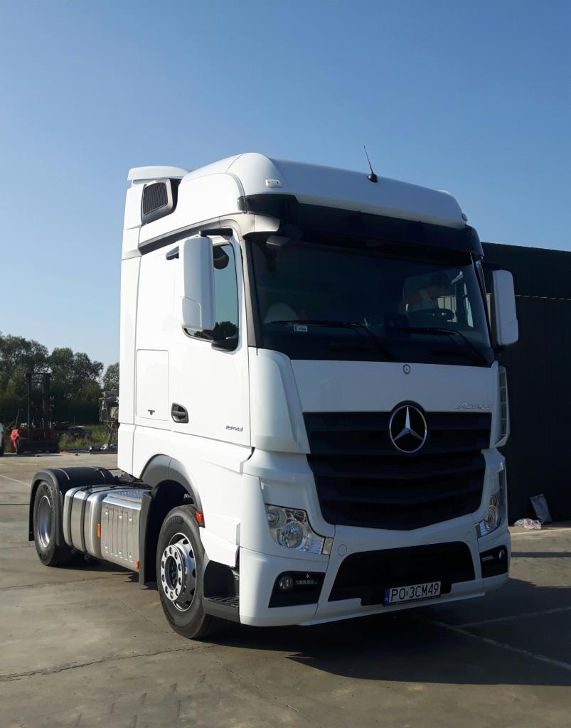 Biały ciągnik siodłowy Mercedes Actros, widok z przodu, zaparkowany na betonowym placu w słoneczny dzień.