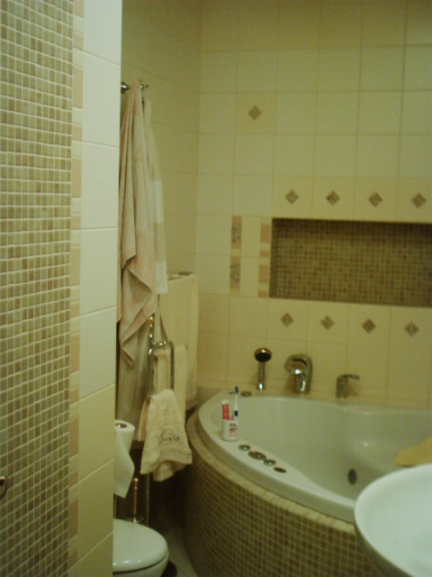 Wykończona łazienka z mozaiką na ścianie i obudowie wanny, widoczna wanna z hydromasażem, toaleta, ręczniki na wieszaku i armatura.