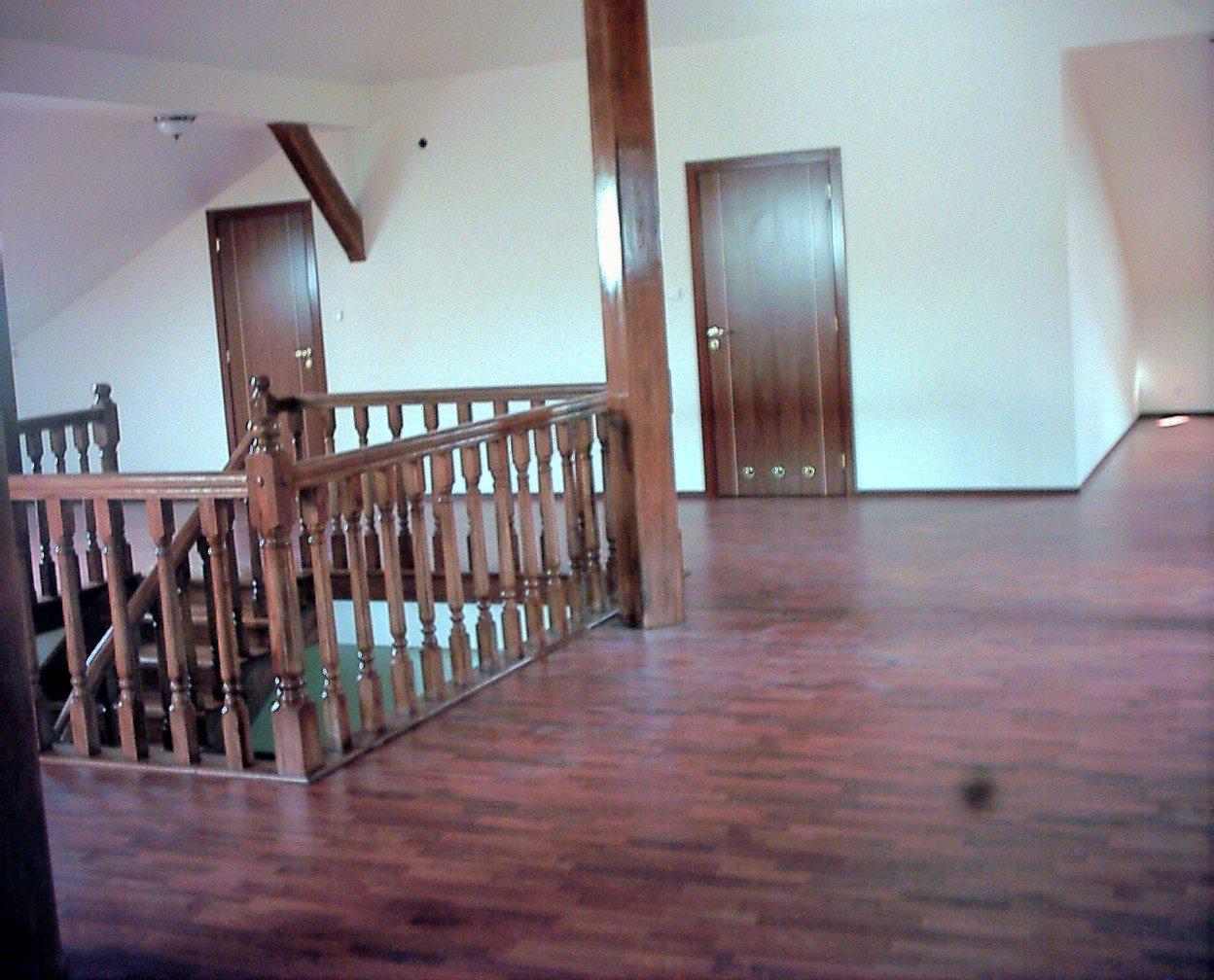 Wykończone poddasze z drewnianymi schodami, balustradą i podłogą, widoczne dwie drewniane drzwi w białych ścianach.