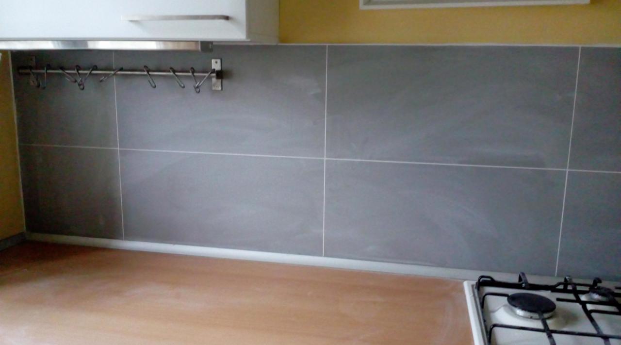 Szare płytki ścienne z białymi fugami nad blatem w kuchni w Łodzi, z relingiem na akcesoria kuchenne zamontowanym na ścianie.