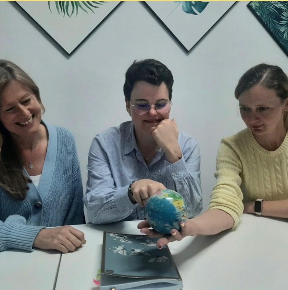 Trzy kobiety przy stole analizują globus, prawdopodobnie podczas lekcji języka obcego.